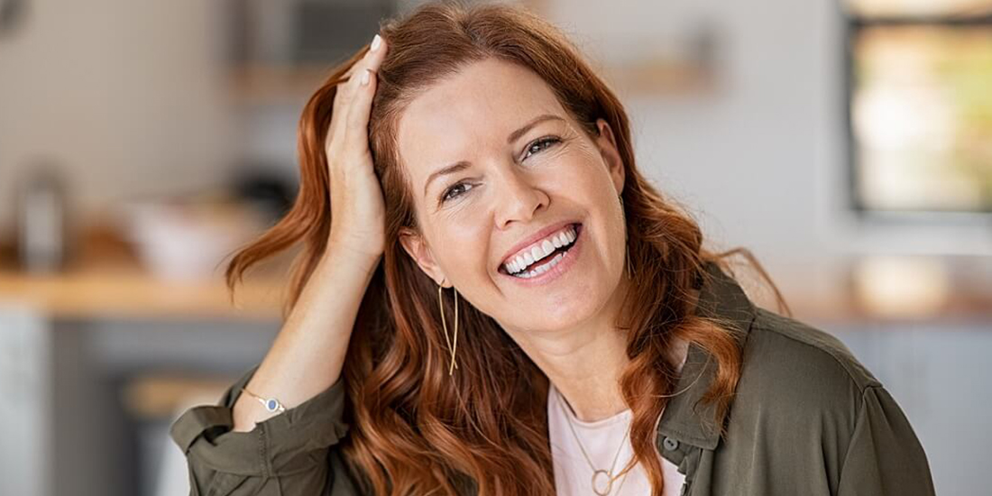 Eine Frau mit langen, roten Haaren stützt ihren Kopf und lacht Eine Frau mit langen, roten Haaren stützt ihren Kopf und lacht